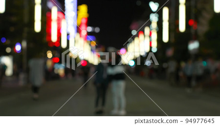 Image of defocussed shop and street lights, with people walking on a city road at night Image of defocussed shop and street lights, with people walking on a city road at night 94977645