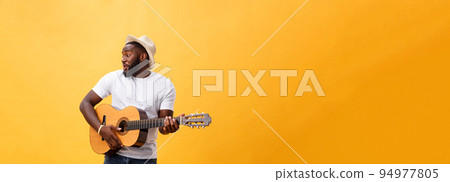 Muscular black man playing guitar, wearing jeans and white tank-top. Isolate over yellow background. Muscular black man playing guitar, wearing jeans and white tank-top. Isolate over yellow background. 94977805