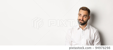 Close-up of doubtful and gloomy man looking left, sighing uncertain, standing over white background Close-up of doubtful and gloomy man looking left, sighing uncertain, standing over white background 94978298