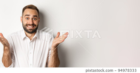 Close-up of awkward manager shrugging and smiling with sorry look, standing clueless over white background Close-up of awkward manager shrugging and smiling with sorry look, standing clueless over white background 94978333