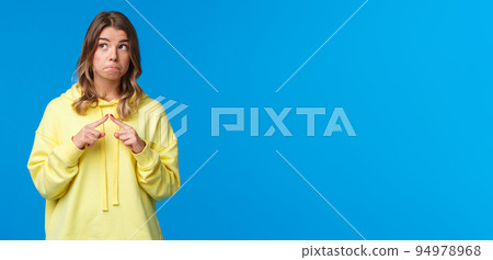 Shy and silly kawaii blond girl in yellow hoodie being modest embarrassed say I love you, poking fingers and look away not to have eye contact as blushing, have something to ask, blue background 94978968