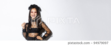 Image of beautiful asian woman in halloween costume, showing credit card and smiling, standing in gothic lace dress over white background Image of beautiful asian woman in halloween costume, showing credit card and smiling, standing in gothic lace dress over white background 94979097