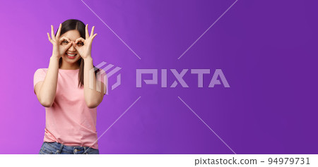 Cheerful friendly carefree asian woman having fun fool around, show okay ok signs on eyes make glasses from fingers, smiling delighted, mimicking funny emotions, stand purple background happy 94979731