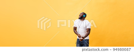 Full length portrait of a cherry young african american man listening to music with headphones and dancing isolated over yellow background 94980087