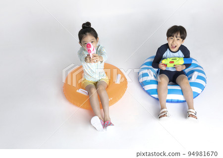Korean boy and girl, summer concept in white background_sitting on the inflatable pool float holding a water gun 94981670
