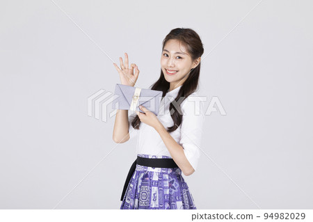 beautiful Korean woman in 20s wearing modern Hanbok_holding a Korean traditional wedding clutch, envelope with ok sign motion 94982029