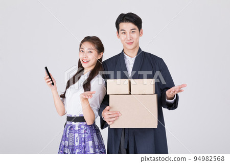 Korean couple_young man and woman in 20s_wearing modern Hanbok_holding smartphone and delivery box 94982568