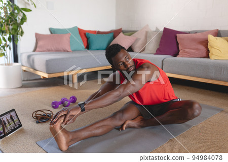 Happy african american man exercising, using tablet in living room 94984078