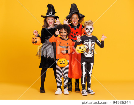 Happy Halloween. Kids in carnival costumes and makeup make a terrible gesture on bright colored yellow background 94986244