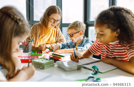 Teacher helping children with schoolwork at school Teacher helping children with schoolwork at school 94986315