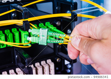 Hand of computer technician connecting fiber optics cable into data switch Hand of computer technician connecting fiber optics cable into data switch 94986341