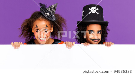 Happy Halloween. Ethnic kids in carnival costumes and makeup with blank white poster on colored purple background Happy Halloween. Ethnic kids in carnival costumes and makeup with blank white poster on colored purple background 94986388