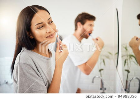 Makeup, face and beauty with a woman using cosmetics in the bathroom at home with her man in the background. Cosmetic, skin and care with an attractive young female and her boyfriend in their house 94988356