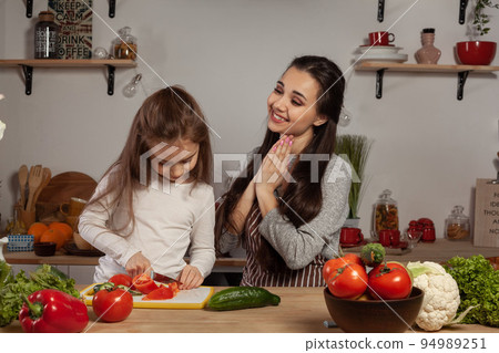 Mother and her daughter are making a vegetable salad and having fun at the kitchen. 94989251