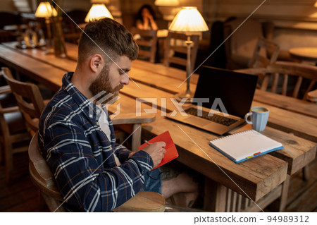 Casual business man or freelancer planning his work on notebook, working on laptop computer with smart phone, cup of coffee on table at coffee shop or home office. 94989312