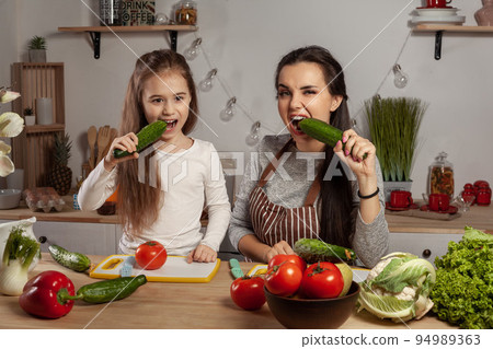 Mother and her daughter are making a vegetable salad and having fun at the kitchen. 94989363