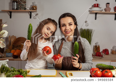 Mother and her daughter are making a vegetable salad and having fun at the kitchen. Mother and her daughter are making a vegetable salad and having fun at the kitchen. 94989384