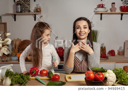 Mother and her daughter are making a vegetable salad and having fun at the kitchen. 94989415