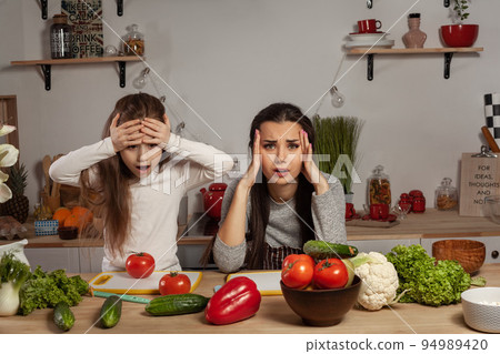 Mother and her daughter are making a vegetable salad and having fun at the kitchen. Mother and her daughter are making a vegetable salad and having fun at the kitchen. 94989420