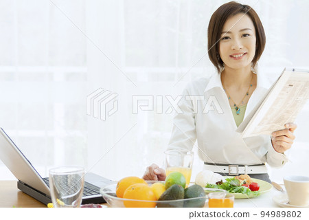 Woman having breakfast while reading newspaper 94989802