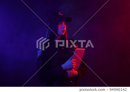 Redheaded female police officer is posing for the camera against a black background with red and blue backlighting. 94990142