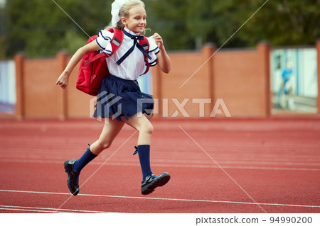 Start. Back to school, kids and education concept. Girl dressed in school uniform as elementary student carrying big backpack running on treadmill at the stadium or arena. Start. Back to school, kids and education concept. Girl dressed in school uniform as elementary student carrying big backpack running on treadmill at the stadium or arena. 94990200