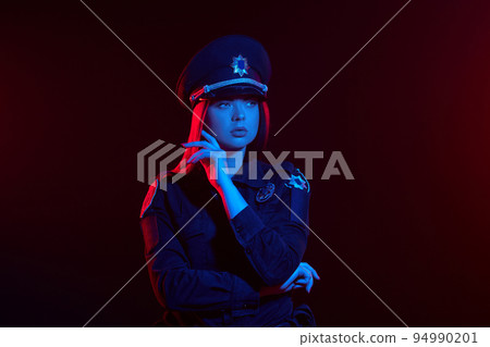 Close-up shot of a redheaded female police officer is posing for the camera against a black background with red and blue backlighting. 94990201