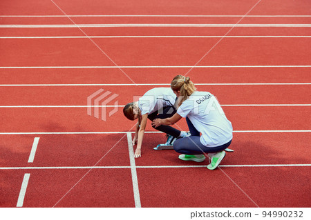 Female coach training athlete. Fit girl getting ready to run on treadmill at the stadium. Concept of sport, achievements, studying, goals, skills. Little teen girl training outdoor. Female coach training athlete. Fit girl getting ready to run on treadmill at the stadium. Concept of sport, achievements, studying, goals, skills. Little teen girl training outdoor. 94990232