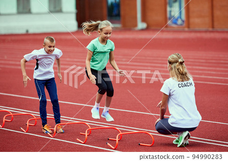 Female coach training athletes. Group of children running on treadmill at the stadium. Concept of sport, achievements, studying, goals, skills. Little boys and girls training outdoor. Female coach training athletes. Group of children running on treadmill at the stadium. Concept of sport, achievements, studying, goals, skills. Little boys and girls training outdoor. 94990283