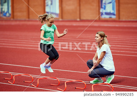 Female coach training athlete. Fit girl getting ready to run on treadmill at the stadium. Concept of sport, achievements, studying, goals, skills. Little teen girl training outdoor. Female coach training athlete. Fit girl getting ready to run on treadmill at the stadium. Concept of sport, achievements, studying, goals, skills. Little teen girl training outdoor. 94990285