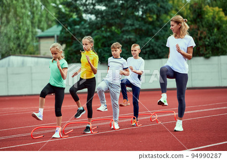 Female coach training athletes. Group of children running on treadmill at the stadium. Concept of sport, achievements, studying, goals, skills. Little boys and girls training outdoor. Female coach training athletes. Group of children running on treadmill at the stadium. Concept of sport, achievements, studying, goals, skills. Little boys and girls training outdoor. 94990287