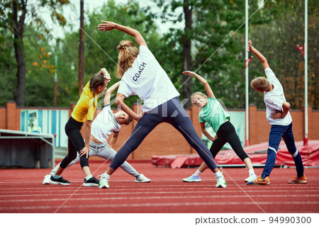 Female coach training athletes. Group of children running on treadmill at the stadium. Concept of sport, achievements, studying, goals, skills. Little boys and girls training outdoor. Female coach training athletes. Group of children running on treadmill at the stadium. Concept of sport, achievements, studying, goals, skills. Little boys and girls training outdoor. 94990300