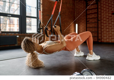 Woman doing arm exercises with trx suspension straps Woman doing arm exercises with trx suspension straps 94990482