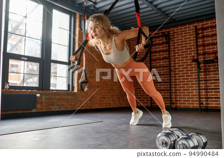 Woman doing arm exercises with trx suspension straps Woman doing arm exercises with trx suspension straps 94990484