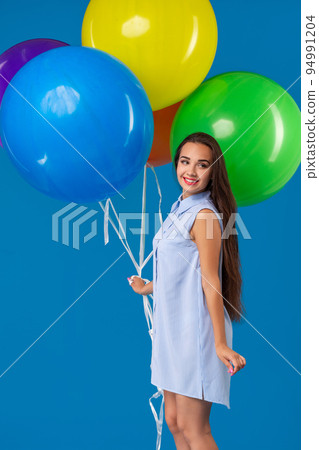 Smiling young woman looking camera and holding colorful air balloons isolated over blue Smiling young woman looking camera and holding colorful air balloons isolated over blue 94991204