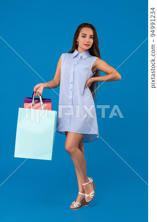 Beautiful young woman holding shopping bags and looking at the camera while standing against blue background. 94991234