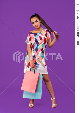 Beautiful young woman holding shopping bags and looking at the camera while standing against purple background. 94991281