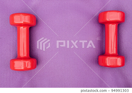 Ladie's dumbbells over purple fitness mat, top view. Copy-space Ladie's dumbbells over purple fitness mat, top view. Copy-space 94991303