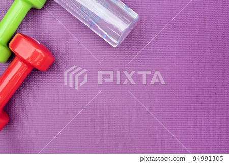 Ladie's dumbbells and water bottle over purple fitness mat, top view. Copy-space Ladie's dumbbells and water bottle over purple fitness mat, top view. Copy-space 94991305