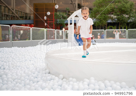 Happy little girl playing white plastic balls pool in amusement park. playground for kids. 94991796