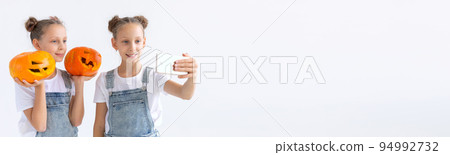 Banner happy Halloween, holidays and childhood concept - Cute little twins sisters girls with a pumpkins Jack-o'-lantern having fun while spending time indoors copy space 94992732