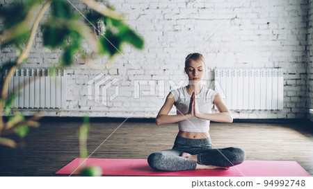 Attractive slim girl is practicing yoga in easy lotus pose on individual session in modern wellness center. Fexibility tranquility meditation concept. 94992748