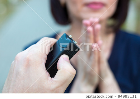 Woman asking for mercy in front of a criminal with a stun gun Woman asking for mercy in front of a criminal with a stun gun 94995131