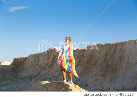 A romantic boy is talking about long-distance travels standing on a mountain with a kite in his hands 94995136