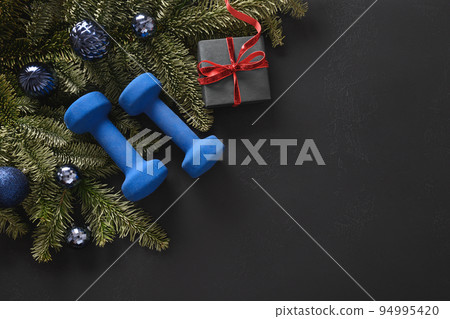 Christmas sport composition with blue sports dumbbells, gift, fir tree branches and Christmas gift Christmas sport composition with blue sports dumbbells, gift, fir tree branches and Christmas gift 94995420