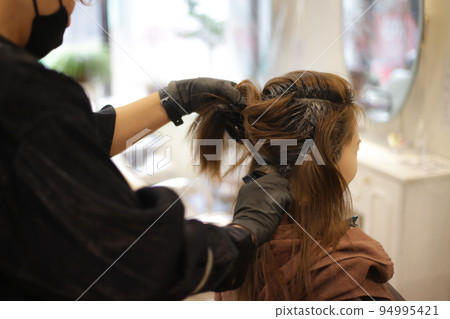 Male hairdresser applying drug to woman's hair 94995421