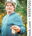 Satisfied young man holding a found porcini mushroom in his hands. The mushroom picker holds a cep mushroom. Man collect mushrooms in forest.  94997080