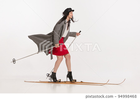 Portrait of young stylish woman in coat standing on skis over white studio background. Winter hobby Portrait of young stylish woman in coat standing on skis over white studio background. Winter hobby 94998468
