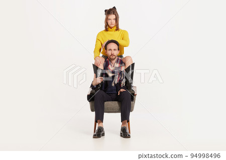 Portrait of brutal man in autumn coat and cap sitting on chair and stylish girl in yellow sweater and boots sitting on man's shoulders 94998496