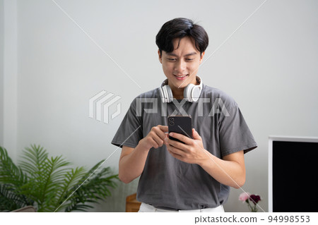 Smiling man using mobile phone and listening music through headphones at home 94998553